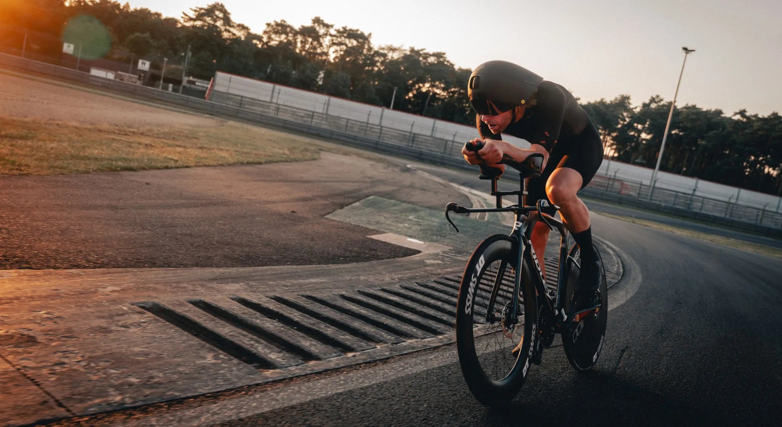 Field testing on Circuit Zolder at sunrise, with an athlete in full aero position wearing Bioracer speedwear, optimizing performance through real-world aerodynamic data collection.