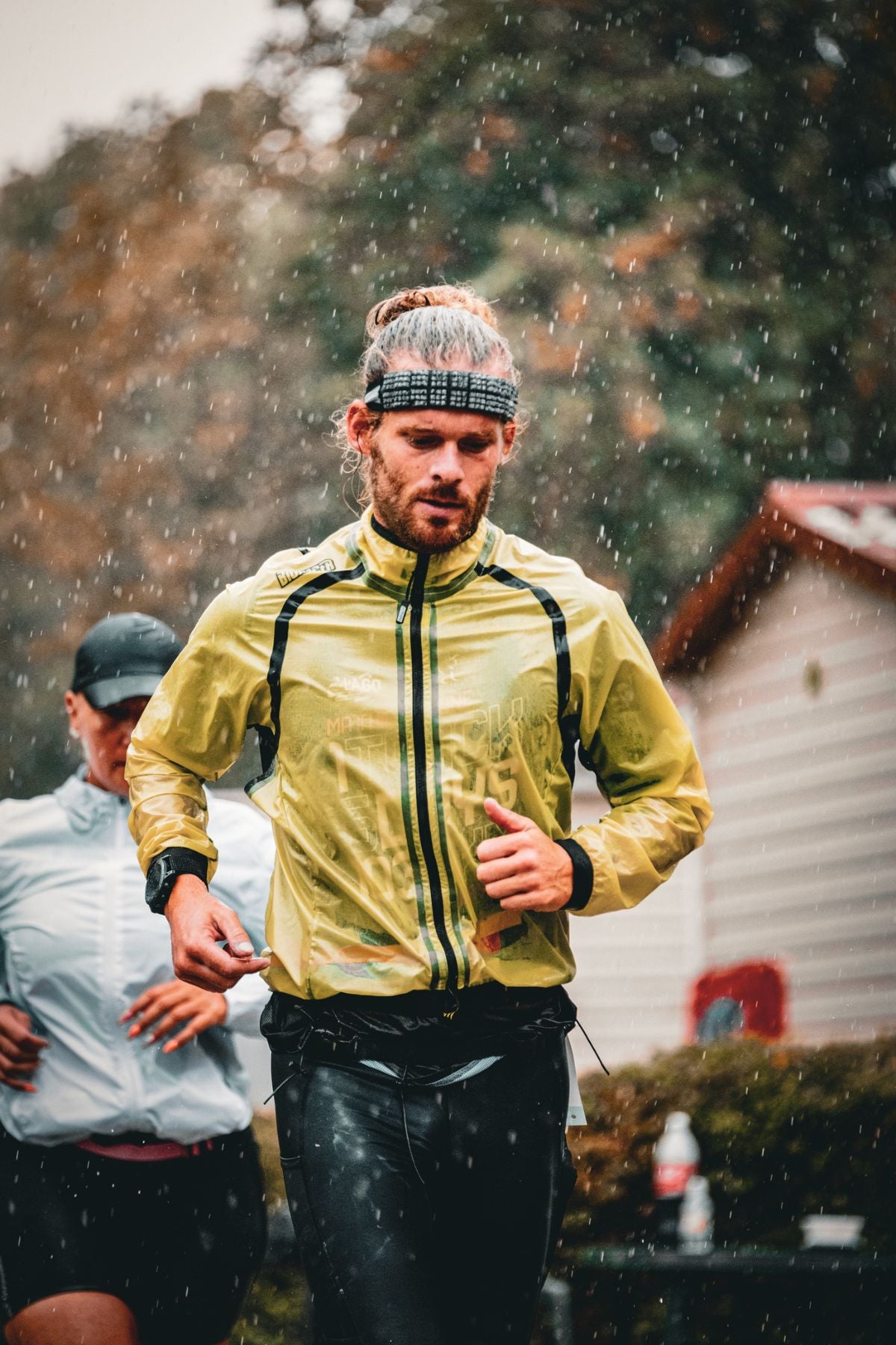 Matthieu Bonne running in the rain during his ultra race, wearing a translucent yellow jacket and black headband, focused and determined.