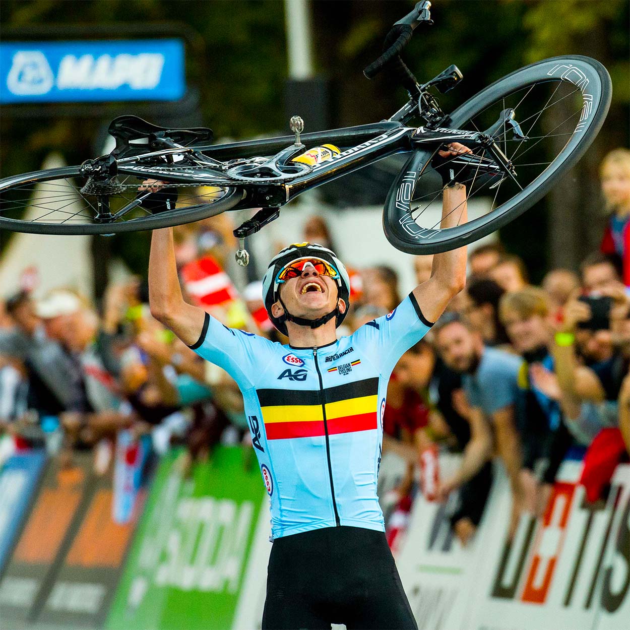 Remco Evenepoel celebrates his dominant victory in the junior road race at the 2018 UCI World Championships, proudly lifting his bike while wearing the Belgian national team kit by Bioracer.