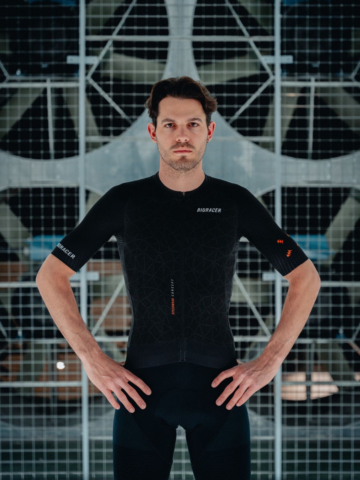 Cyclist in Bioracer Speedwear Graphene black jersey standing in aerodynamic pose inside wind tunnel test facility