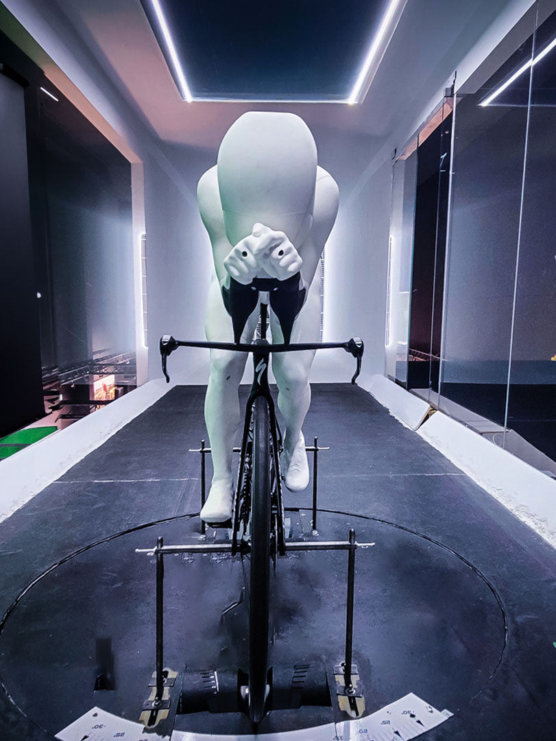 Front view of aerodynamic mannequin on a bike in wind tunnel, used for advanced cycling apparel testing and aero position optimization.