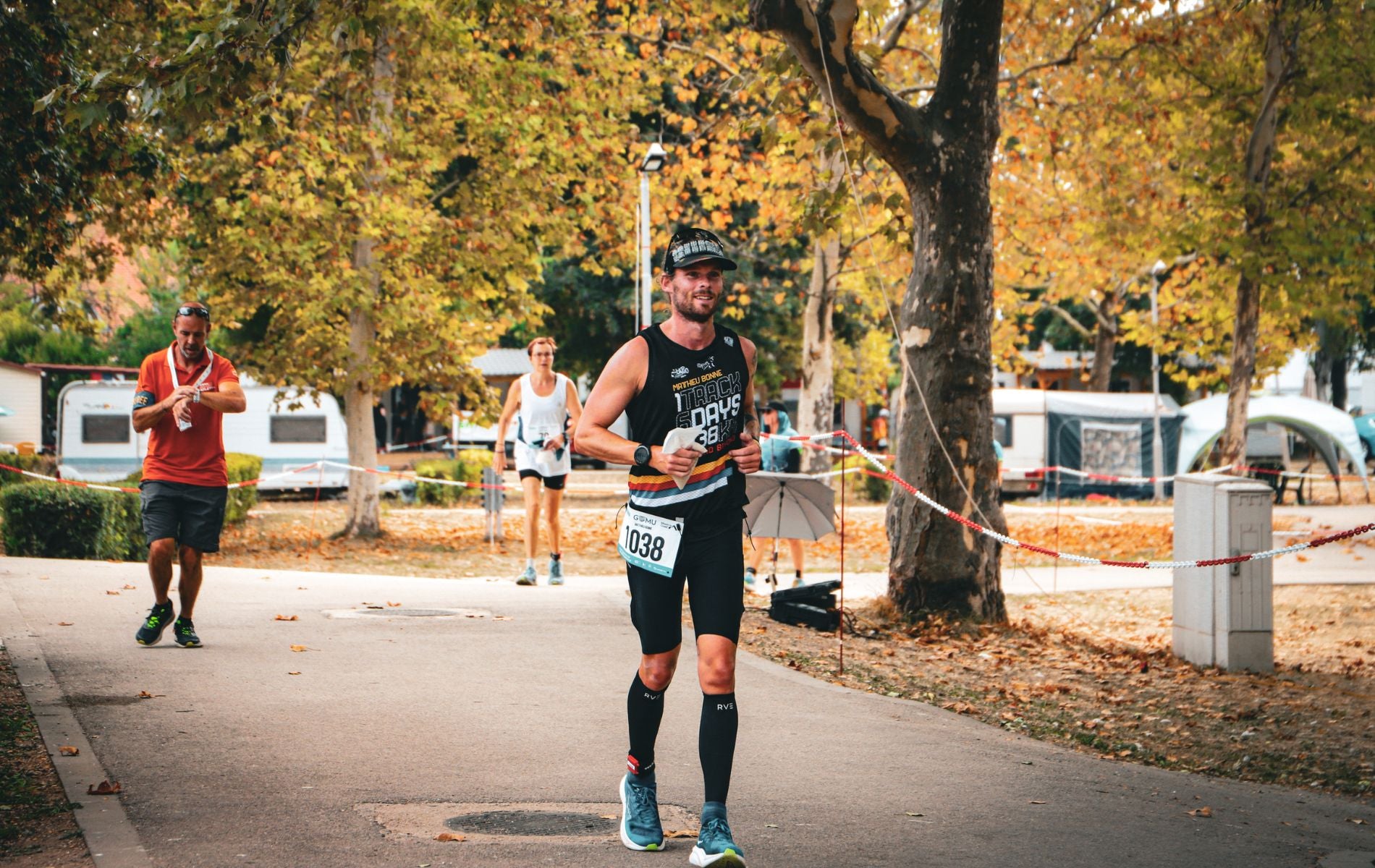 Matthieu Bonne running during his ultra challenge, smiling with race number 1038, surrounded by autumn trees.